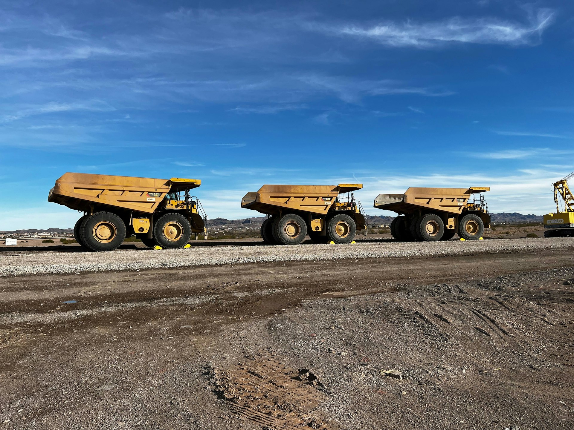 Row of haul trucks parked at a mine site under a blue sky